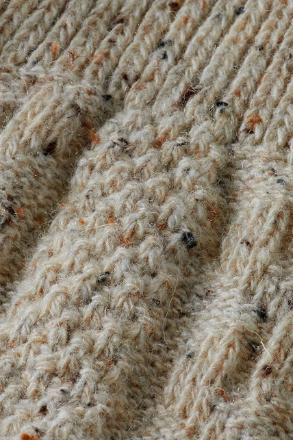 Detail van het gemêleerde beige garen met oranje en zwarte spikkels in de kabelsteek