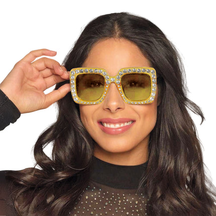 Gouden bril met strass stenen en geel getinte glazen, opgezet door een model