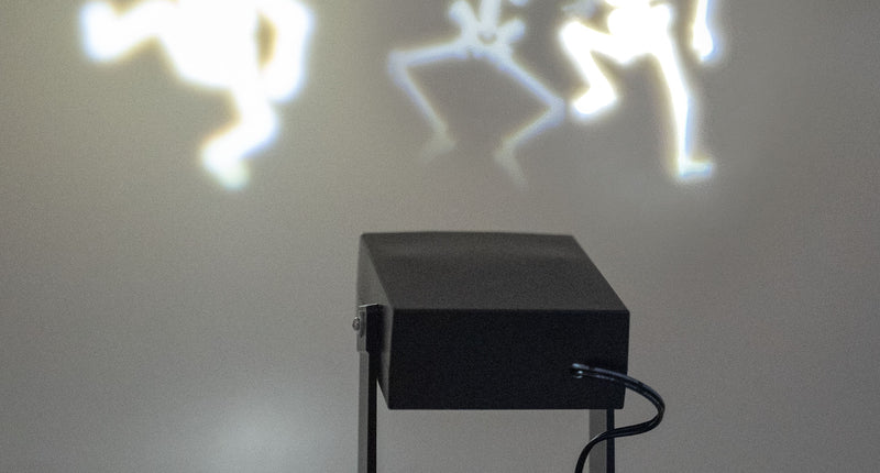 Halloween projector met dansende skeletten in werking, drie witte skeletsilhouetten op de wand tijdens Halloween