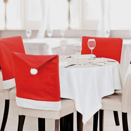 Kerstmuts stoelhoezen met witte pompon aan een gedekte kersttafel met wijnglazen