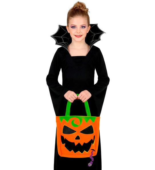 Meisje houdt trick-or-treat tas pompoen vast bij zwarte Halloweenjurk