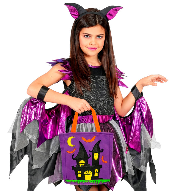 Meisje in vleermuiskostuum met paarse trick-or-treat tas met spookhuisopdruk